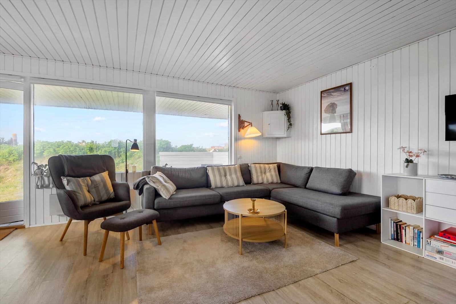 Living room with gray sofa, armchair, and wooden table. Large windows and white walls.