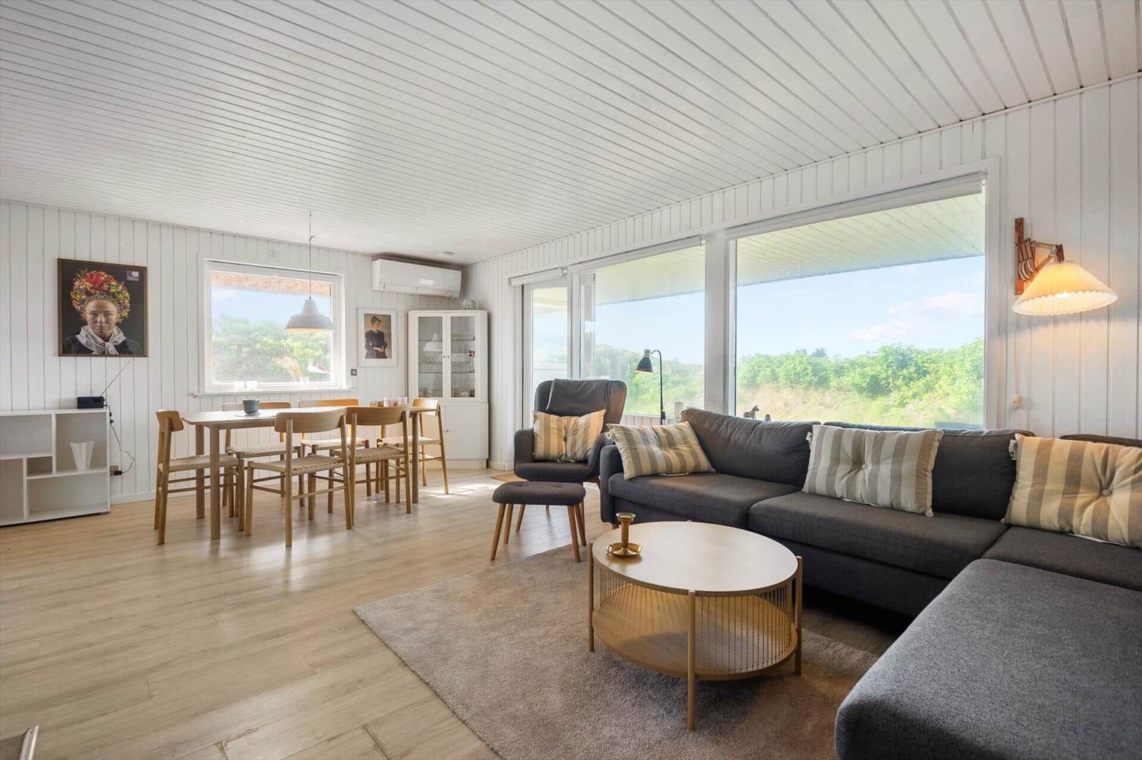 Living and dining area with sofa, table and chairs. Large windows and light walls.