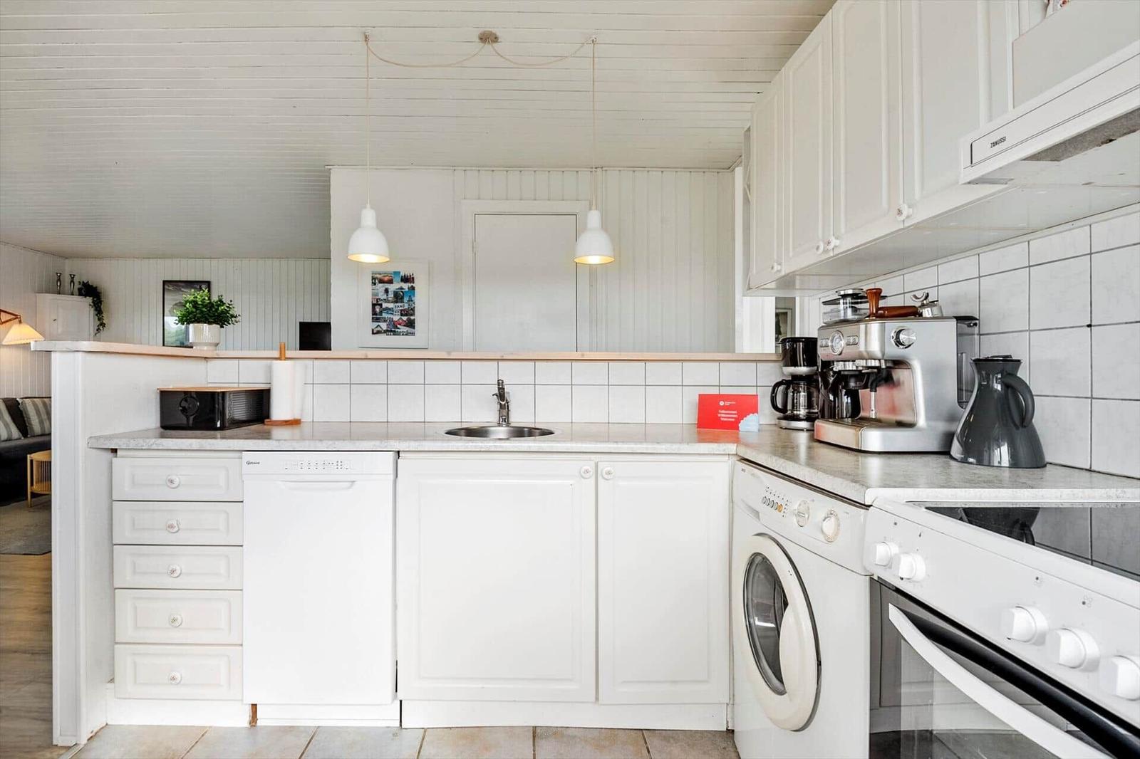 Kitchen with white cabinets, sink, washing machine, and cooking appliances.