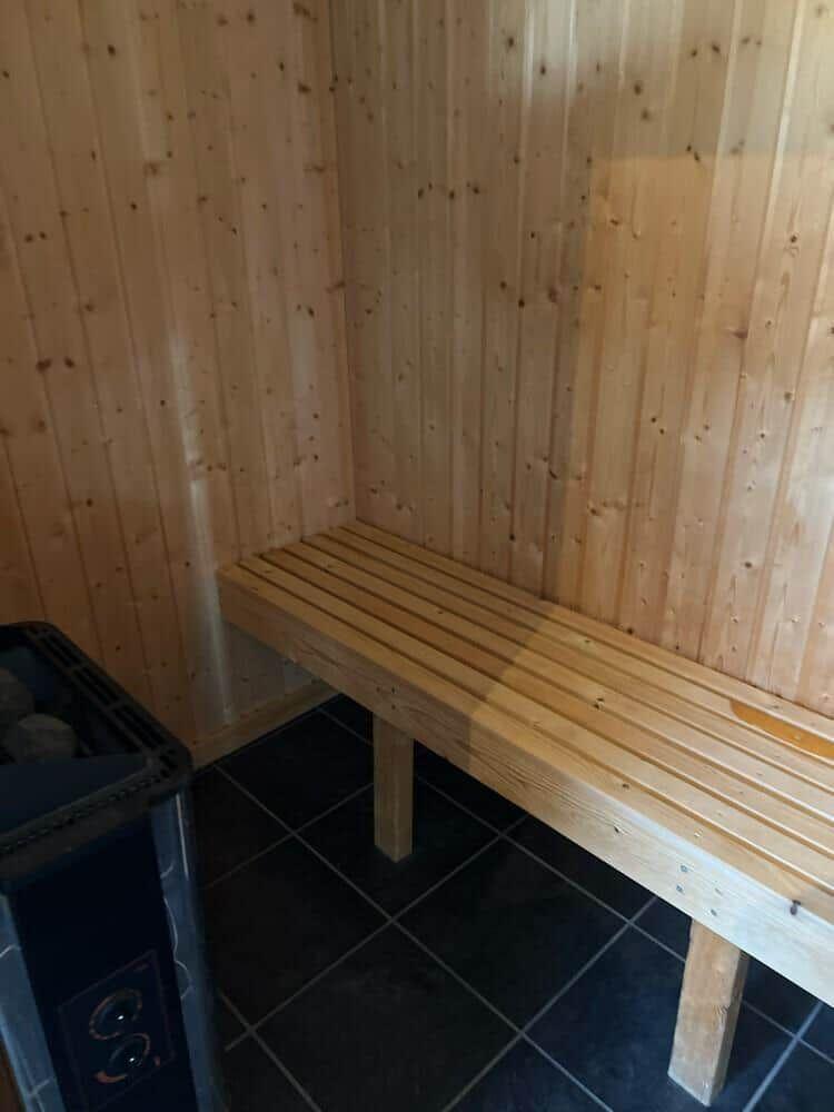 Sauna mit Holzwand und Sitzbank auf dunklem Boden