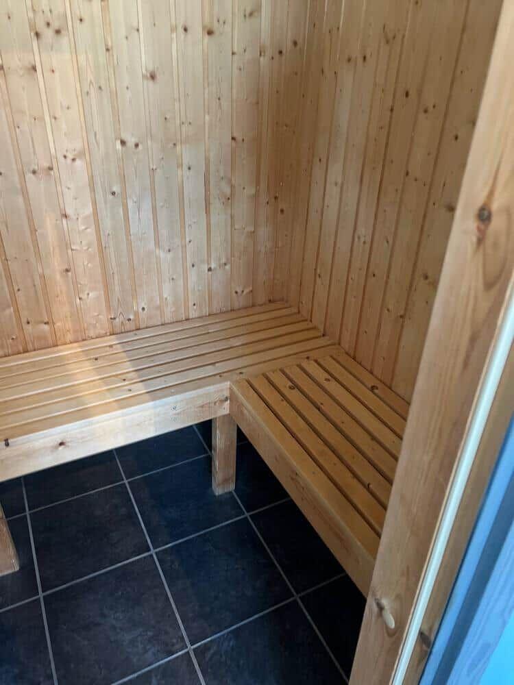 Sauna mit Holzwand und zwei Sitzbänken auf dunklem Boden