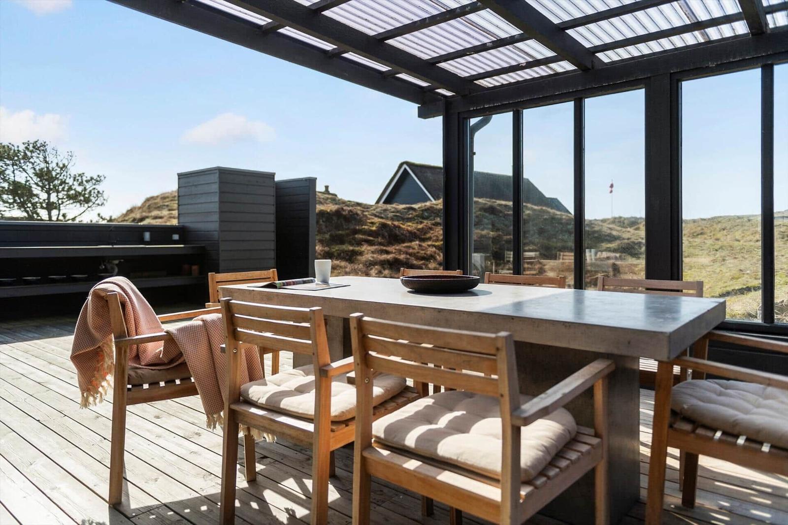Terrasse mit Tisch und Stühlen, Blick auf Hügel und Gebäude.