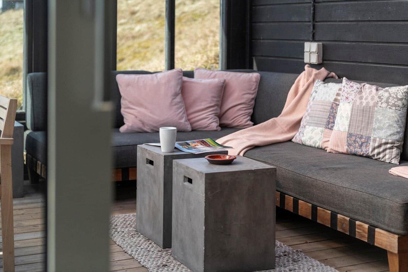 Ein Sofa mit Kissen und Decke vor großen Fenstern. Zwei Betonbeine stehen daneben.