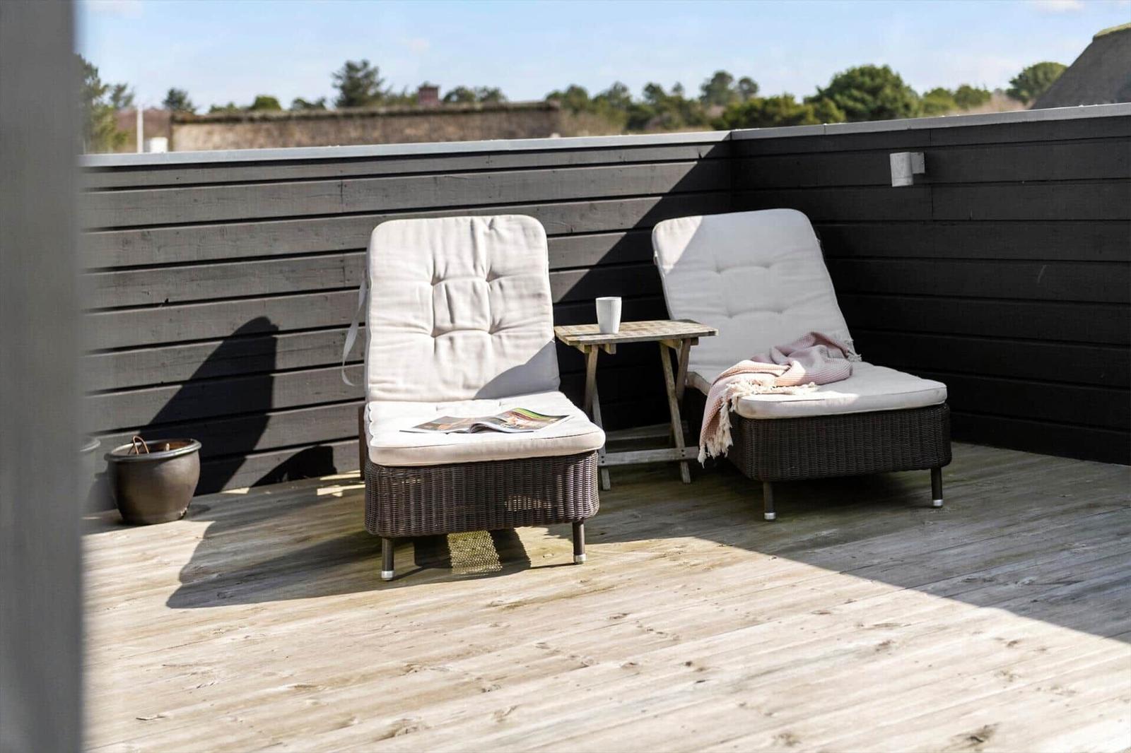Terrasse mit zwei Liegestühlen, Tisch und Holzboden. Hintergrund: Holzwand und Bäume.