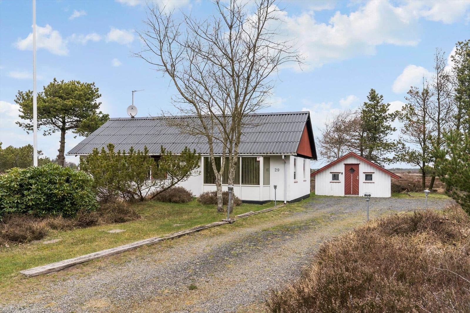 Ein weißes Haus mit grauem Dach und kleiner roter Nebenstelle. Umgeben von Bäumen und Gras.