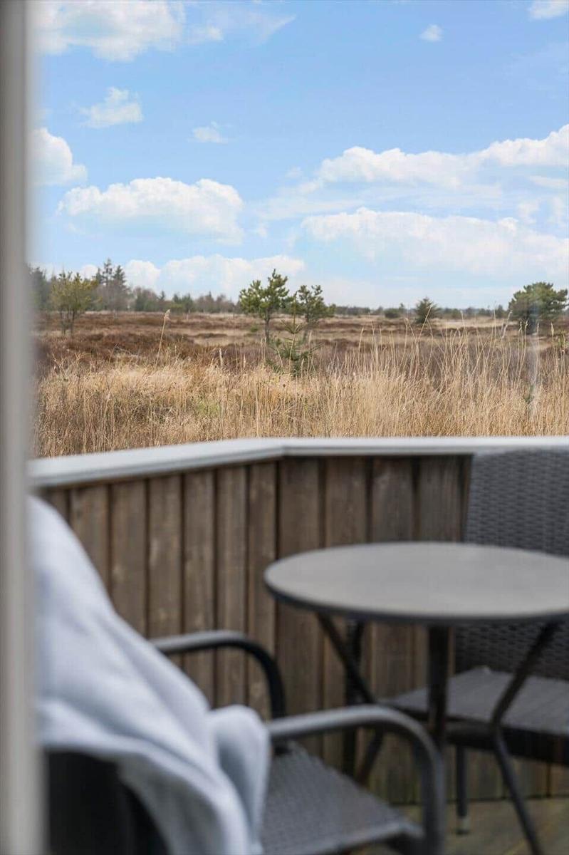 Terrasse mit Tisch und Stühlen, Blick auf trockenes Gras und Himmel mit Wolken.