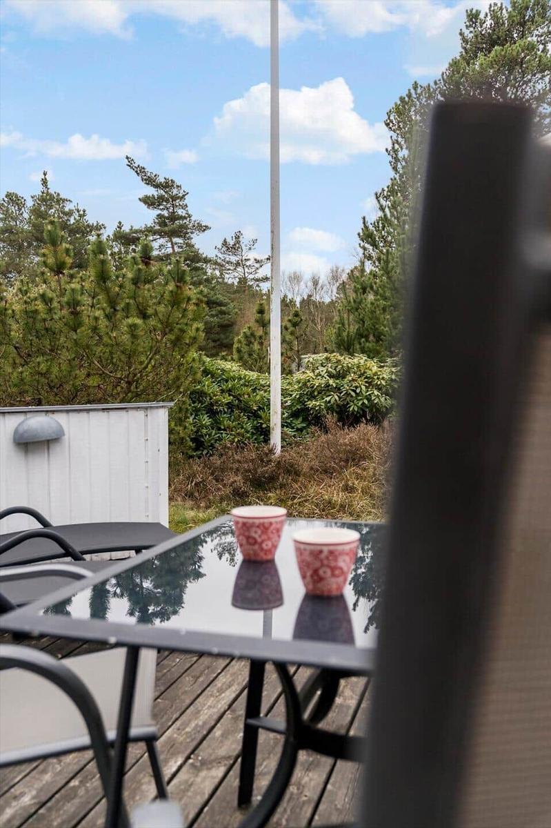 Terrasse mit Tisch, Stühlen und zwei Tassen. Hintergrund: Wald und blauer Himmel.