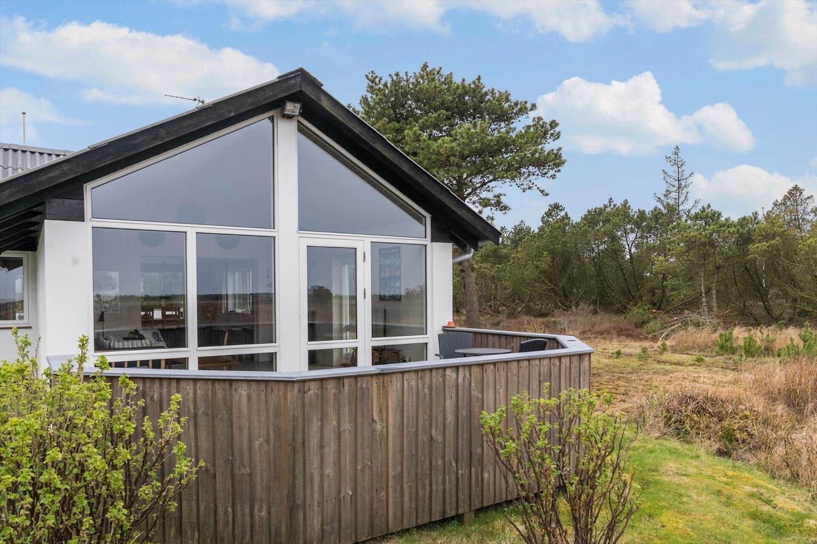 Moderne Ferienhaus mit großem Fensterbereich und Holzumrandung in ländlicher Umgebung.