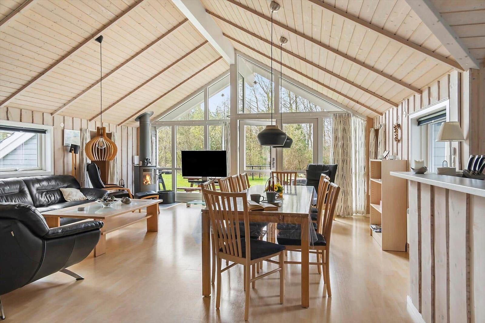 Wohn- und Essbereich mit Holzdecke, Kamin und großem Fenster. Möbel aus Holz und Leder.