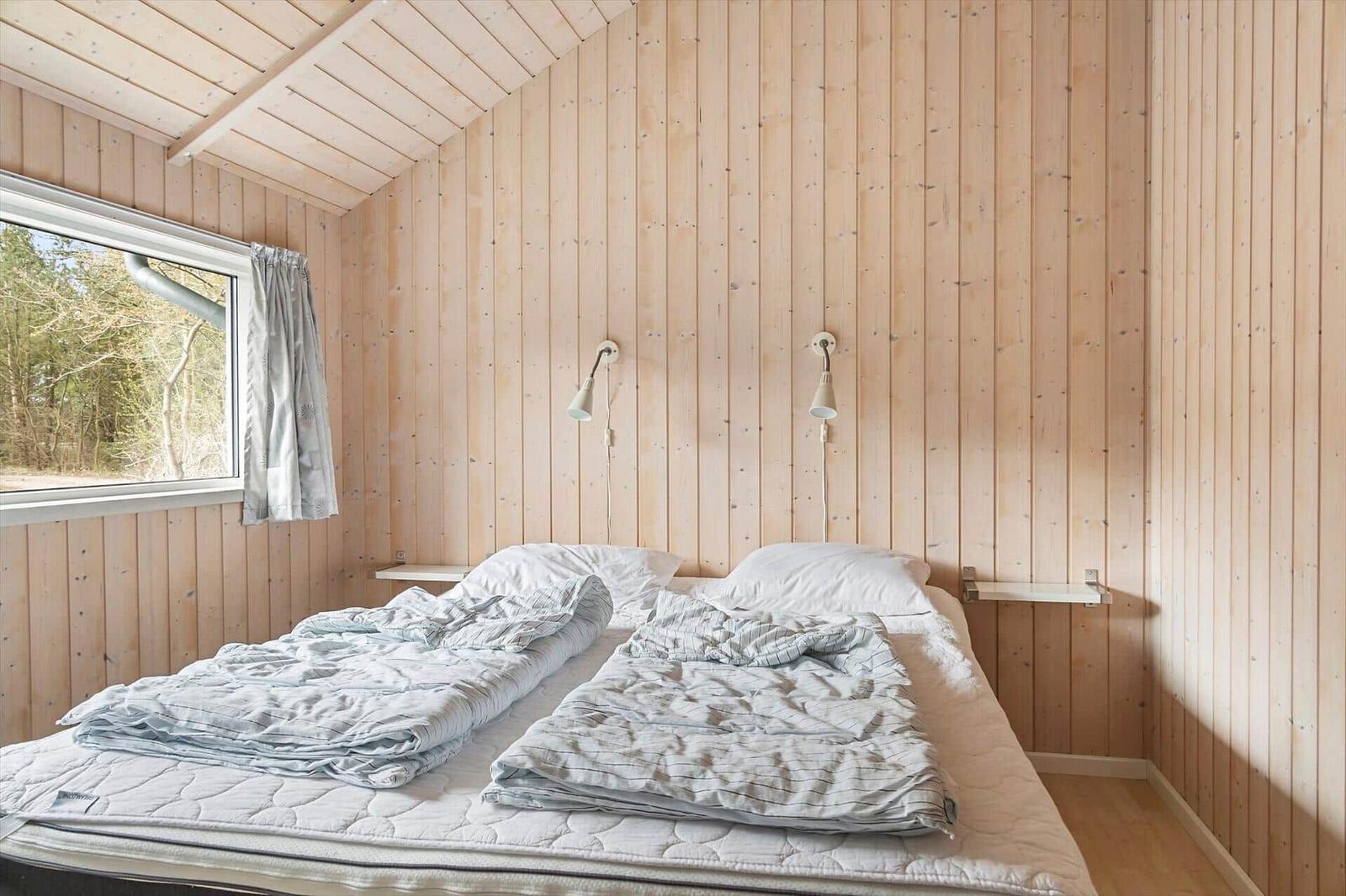 Schlafzimmer mit Holzwand, Bett und Fenster zur Waldansicht.