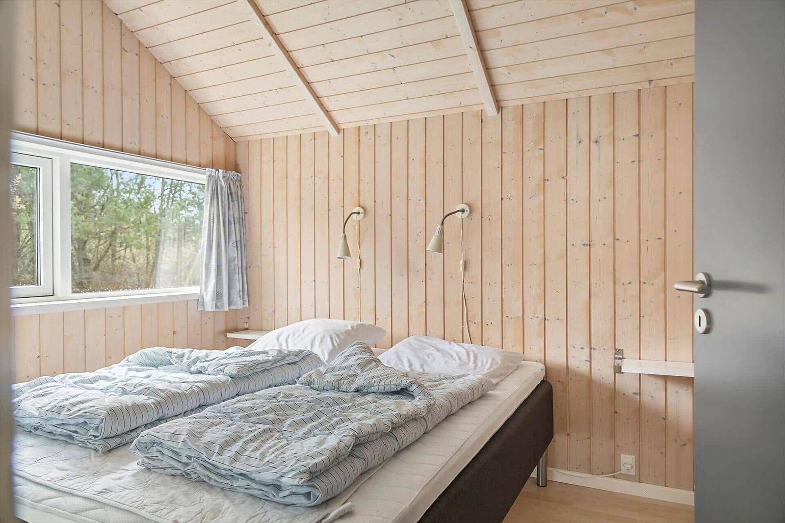 Schlafzimmer mit Holzwand, Bett und Fenster zum Wald.