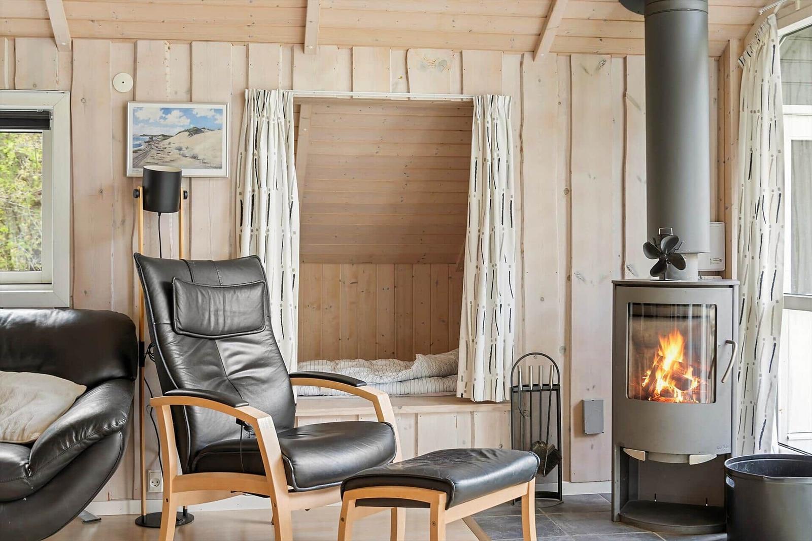 Ein Raum mit Holzwänden, einem Kaminofen und einem Sitzbereich mit Ledersofa und -stuhl.