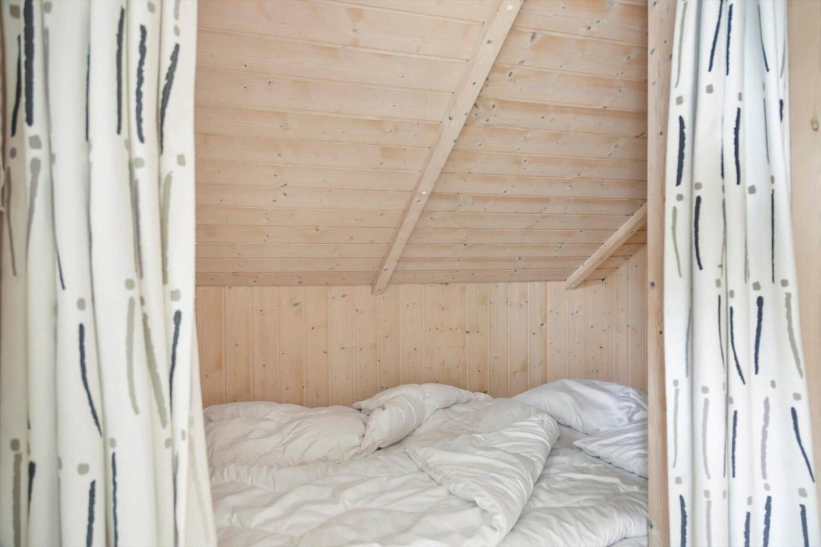 Ein Bett unter einer Holzdecke mit Vorhängen an den Seiten.