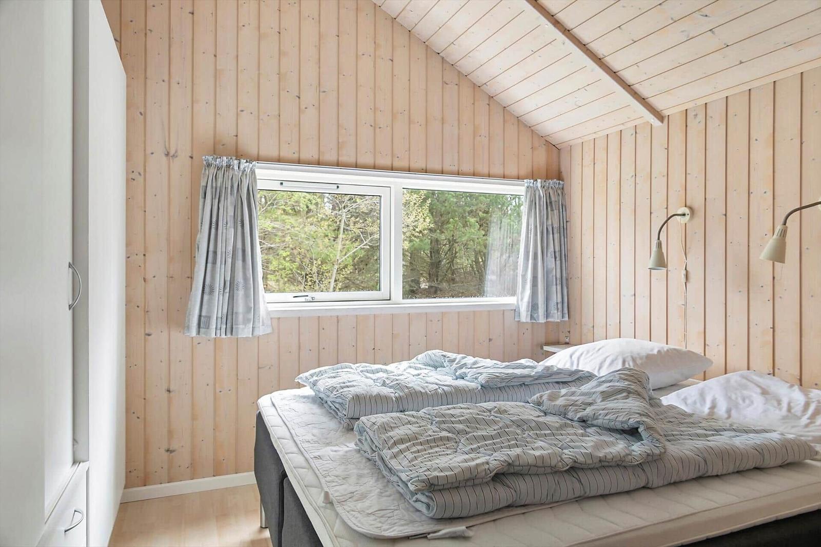 Schlafzimmer mit Holzwand, Fenster und Bett mit Bettwäsche.