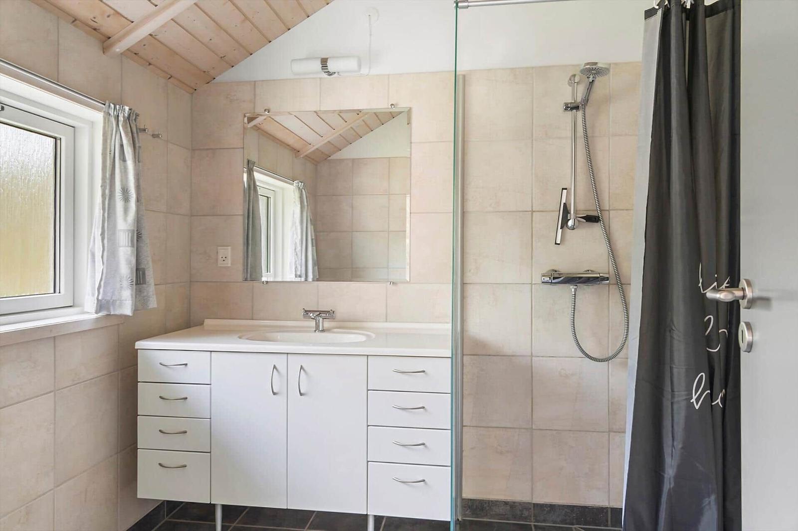 Badezimmer mit Dusche, Waschbecken und Spiegel unter Holzdecke.