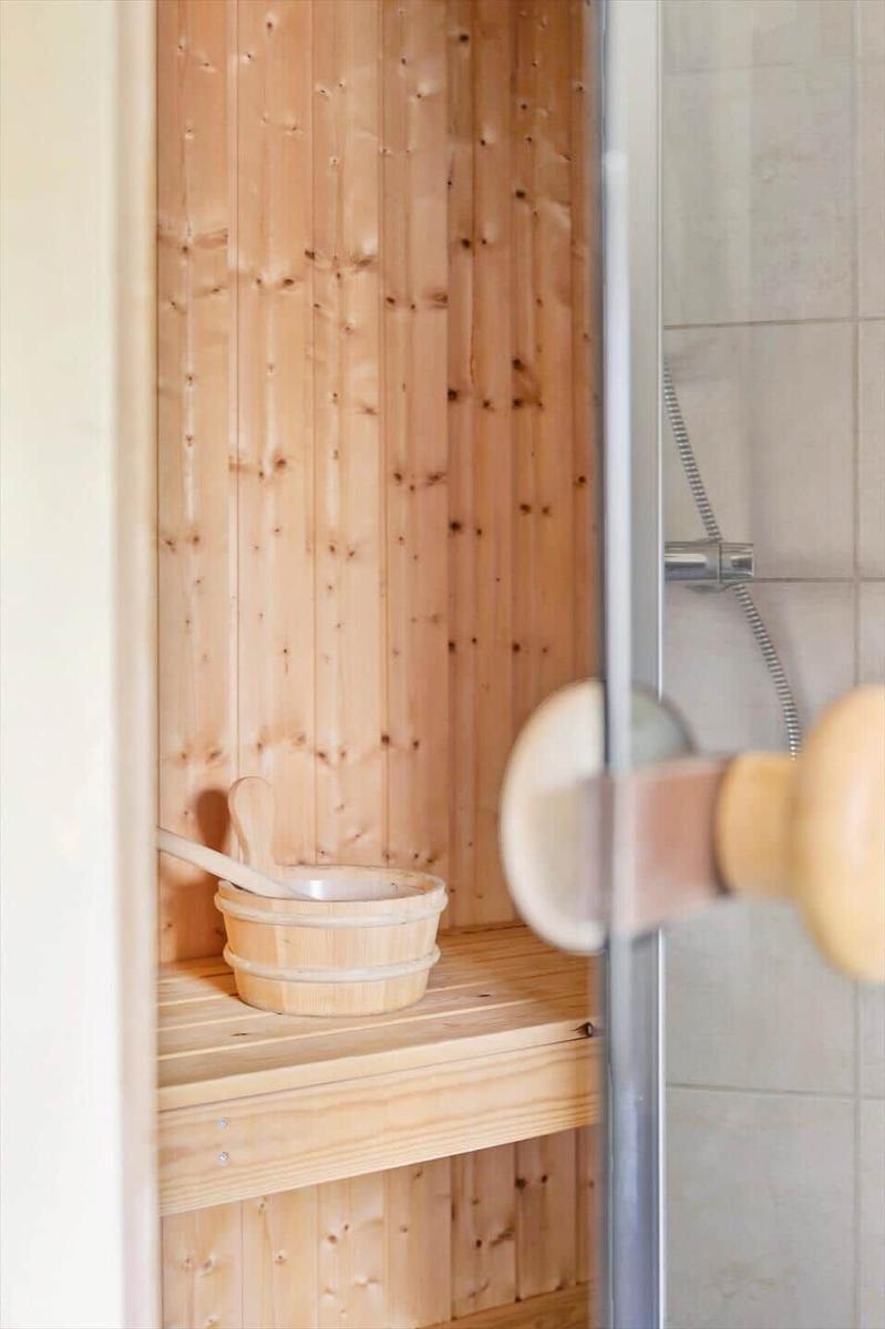 Sauna mit Holzwand und Holzbank, darauf steht ein Holzwaschbecken mit Holzlöffel.