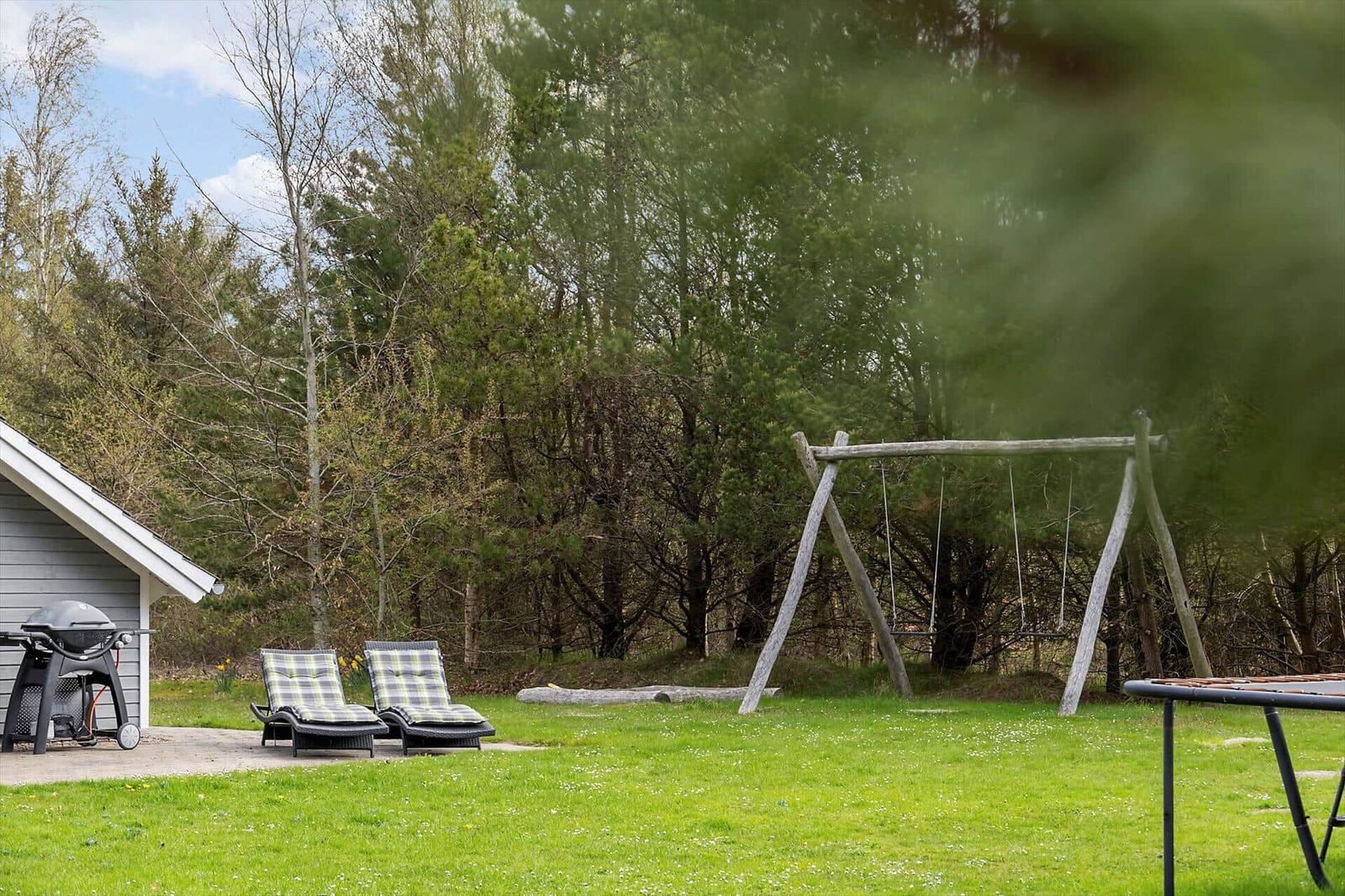 Hinterhof mit Schaukel, Liegestühlen und Grillplatz. Grünfläche und Wald im Hintergrund.