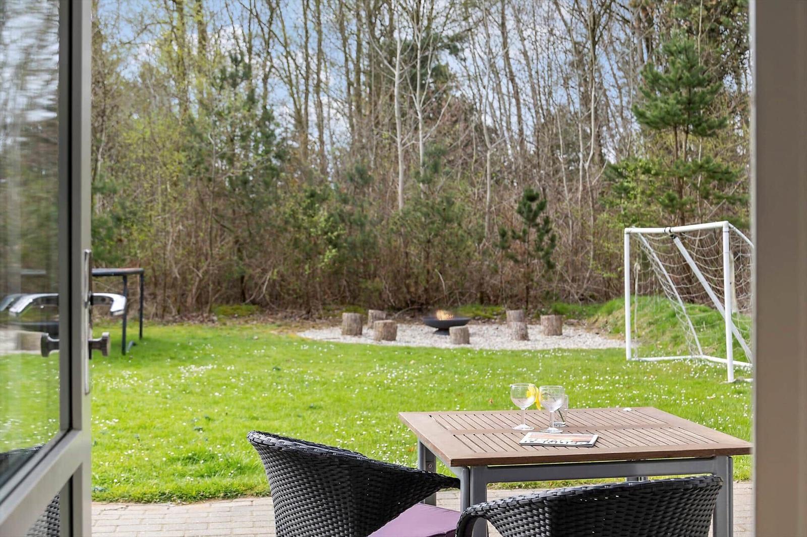 Terrasse mit Tisch und Stühlen, Blick auf grünen Rasen, Feuerkorb und Fußballtor.