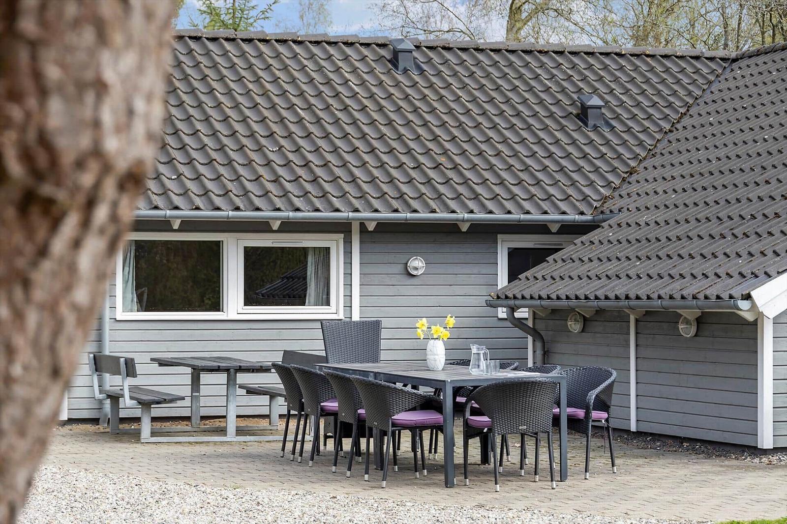 Terrasse mit Tisch und Stühlen vor grauem Holzhaus mit Dachziegeln.