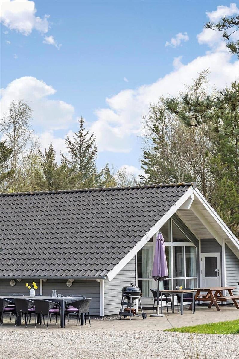 Hütte mit Terrasse, Grill und Tisch unter blauem Himmel mit Bäumen