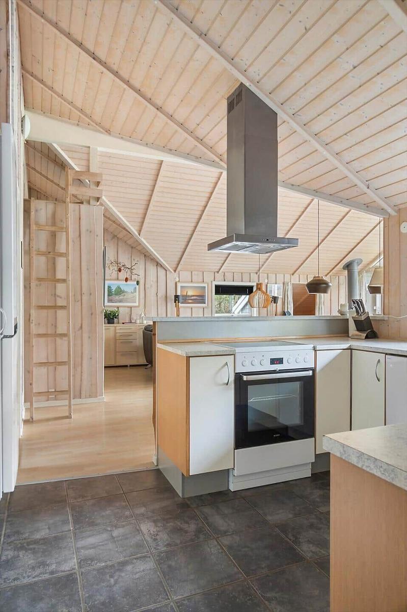 Küche mit Holzdecke, Kochfeld und Ofen. Durchgang zu Wohnbereich mit Holzwand.