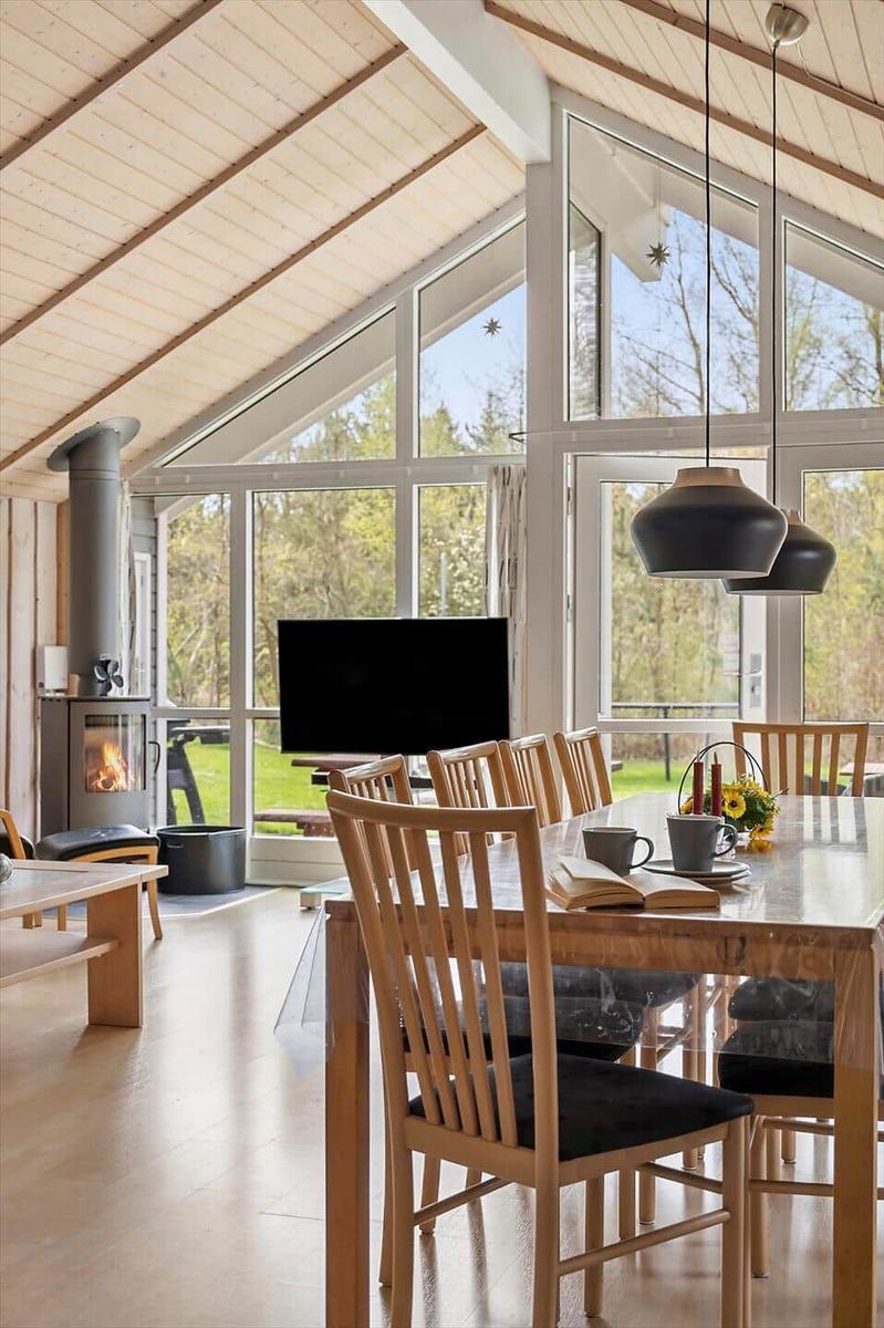 Großes Esszimmer mit Holztisch, Stühlen und Blick auf den Garten. Hohe Decke und große Fenster.