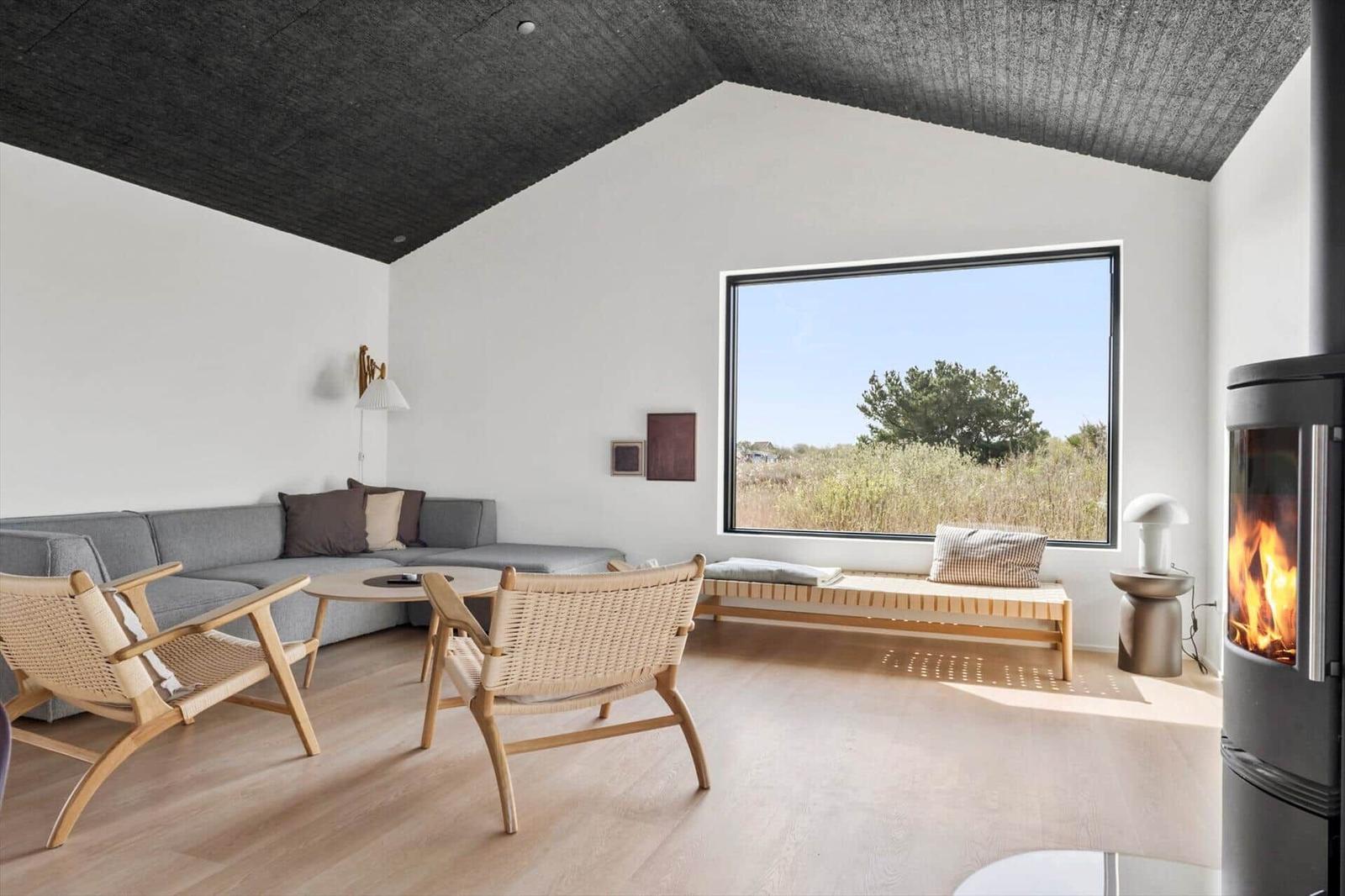 Wohnzimmer mit Sofa, zwei Stühlen, Kamin und großem Fenster mit Blick auf Grasland.