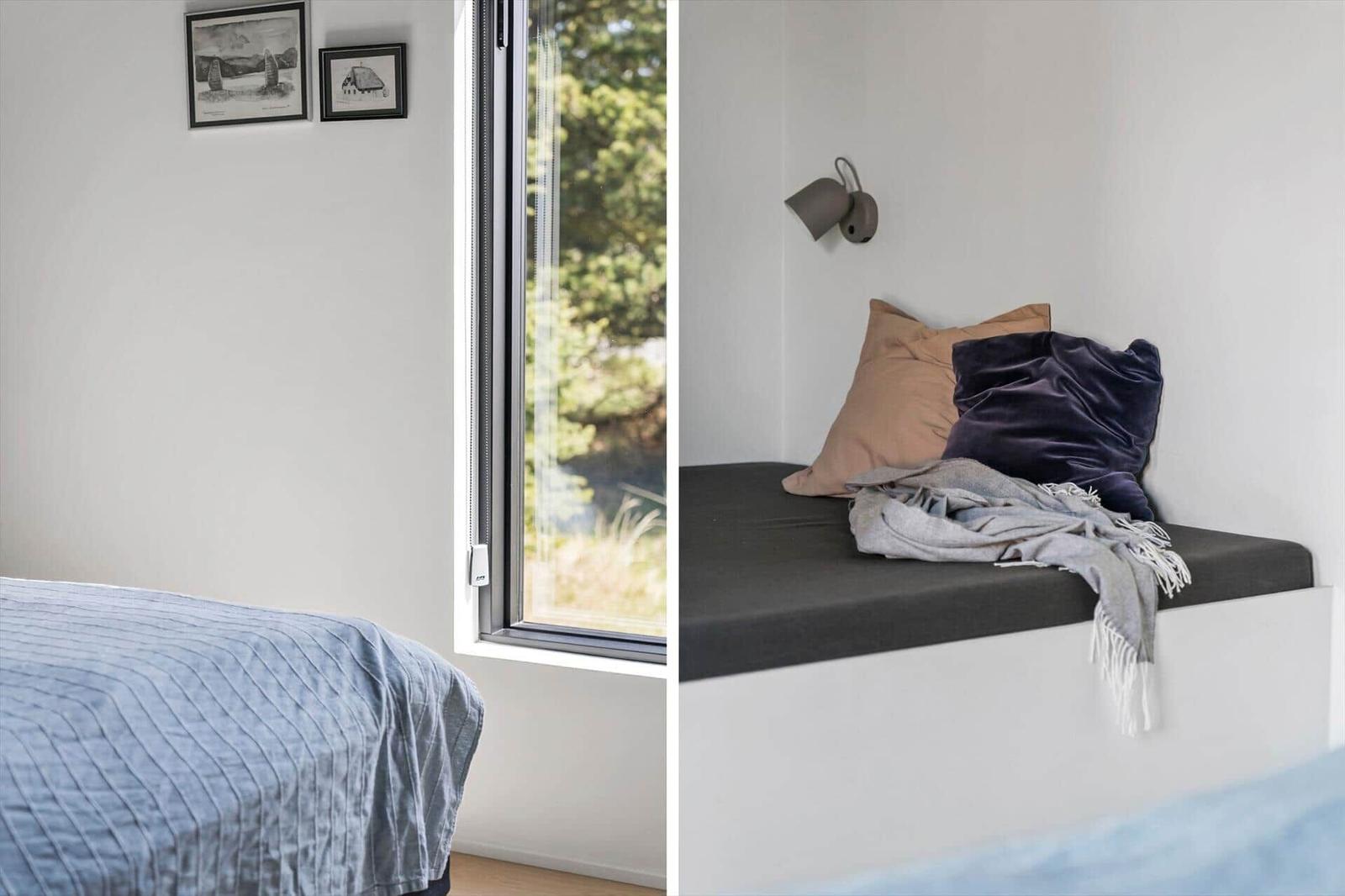 Schlafzimmer mit Bett, Fenster und Wandbildern. Sitzbank mit Kissen und Decke.