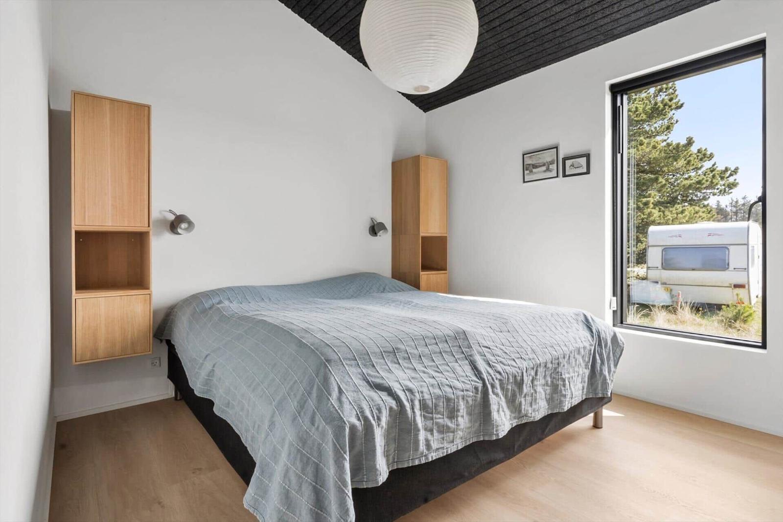 Schlafzimmer mit Bett, Holzregalen und großem Fenster. Blick auf einen Wohnwagen.