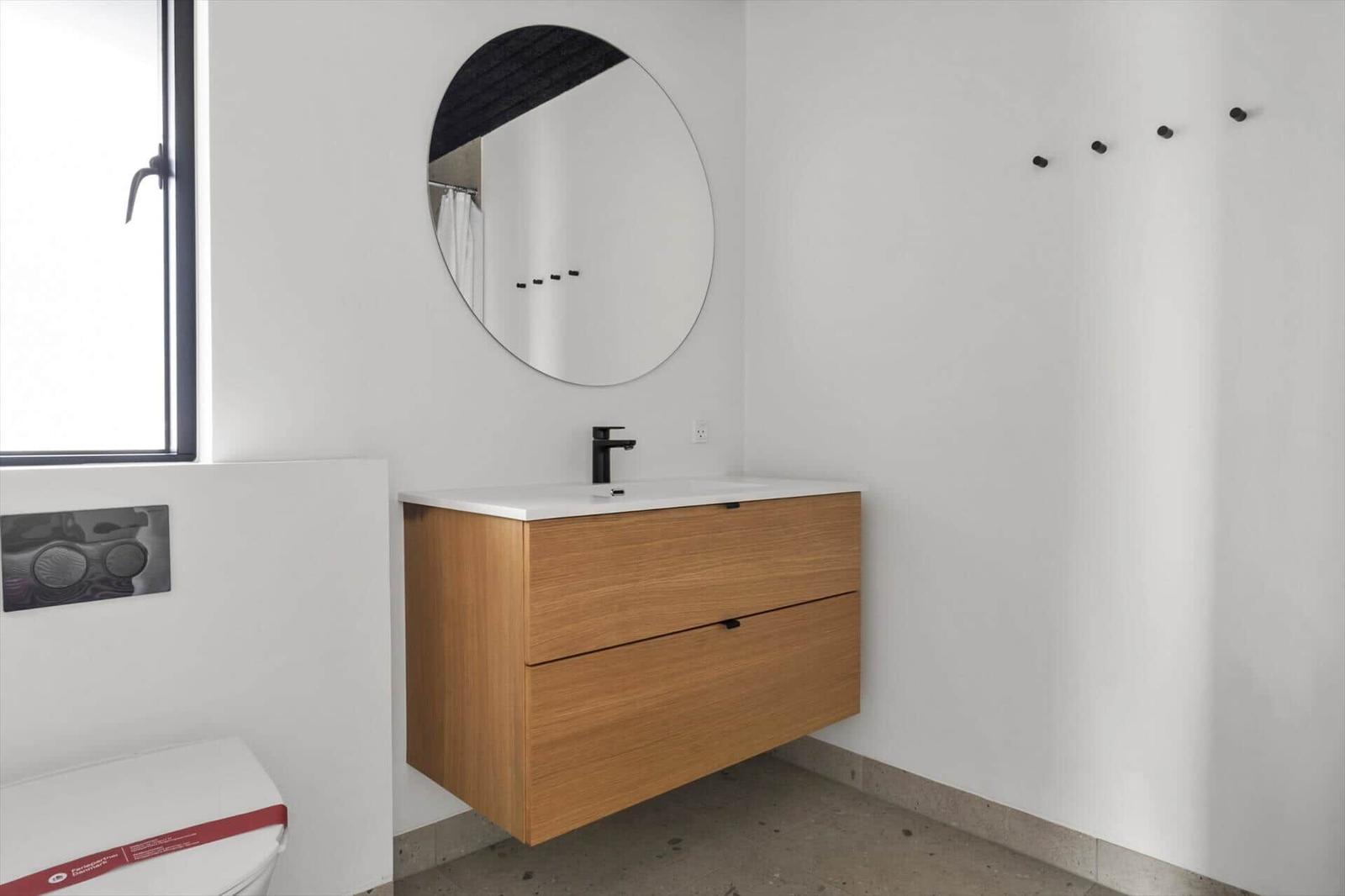 Badezimmer mit Holzwaschbecken, runden Spiegel und Fenster.