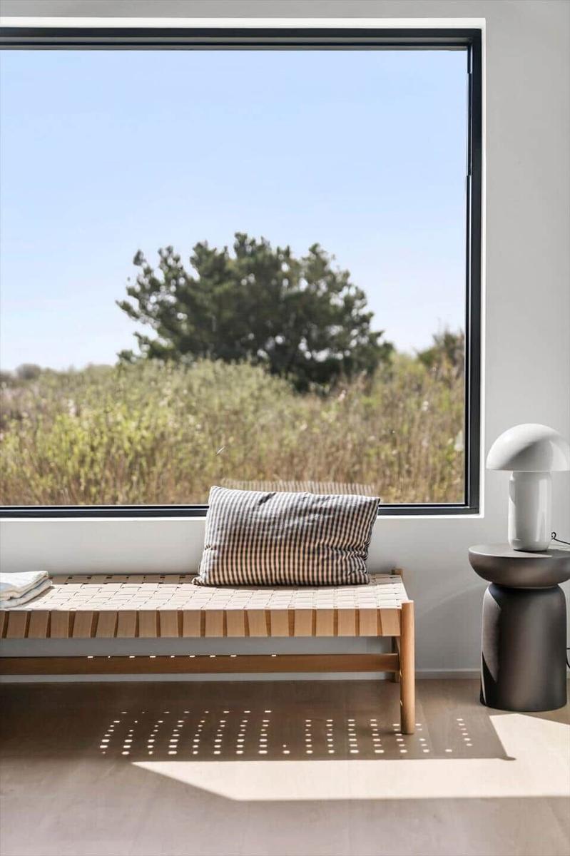 Bank mit Kissen vor großem Fenster mit Blick auf Gras und Baum.