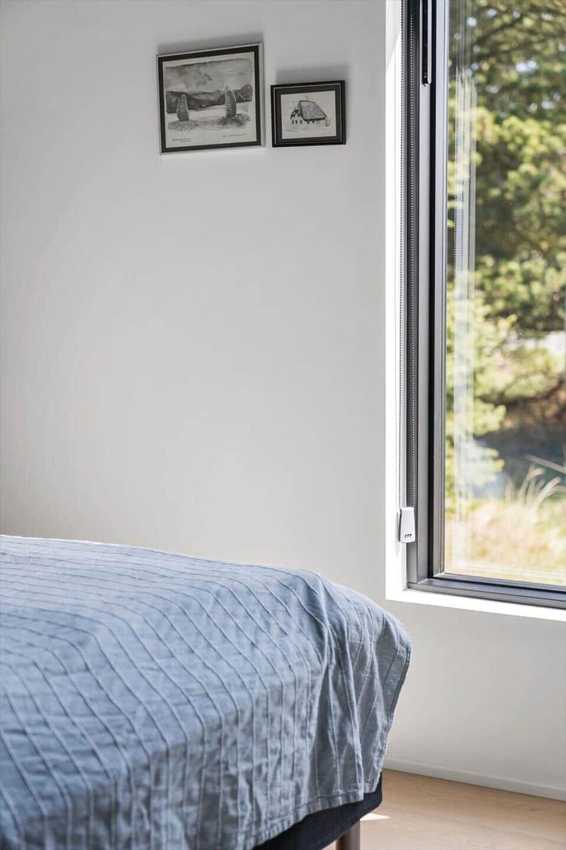 Ein Bett mit blauer Bettdecke neben einem großen Fenster mit Blick auf Bäume.