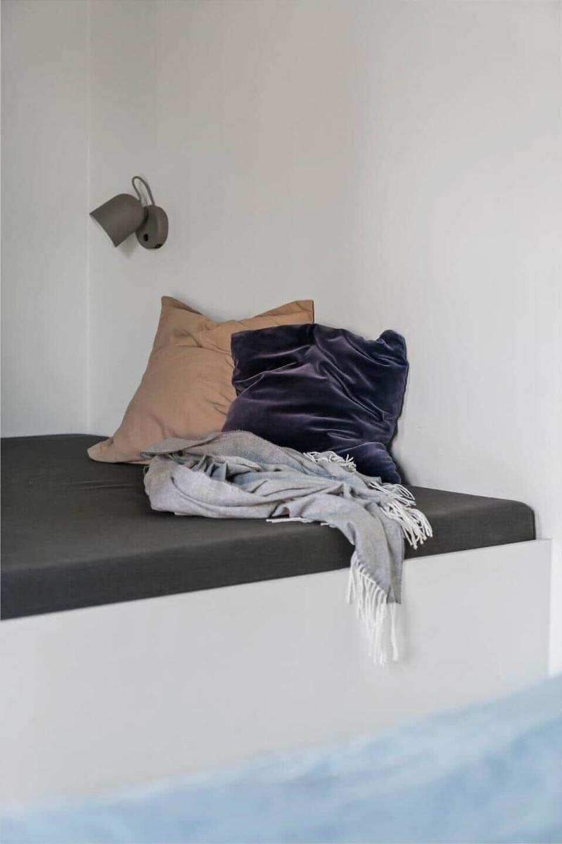 Ein Fensterbank mit Kissen und Decke, Wandlampe und weißer Wand.