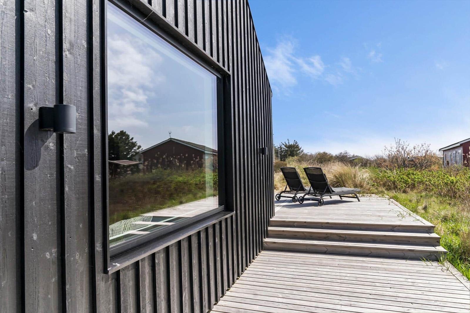 Holzterrasse mit zwei Liegestühlen vor einem modernen Haus mit großen Fenstern.