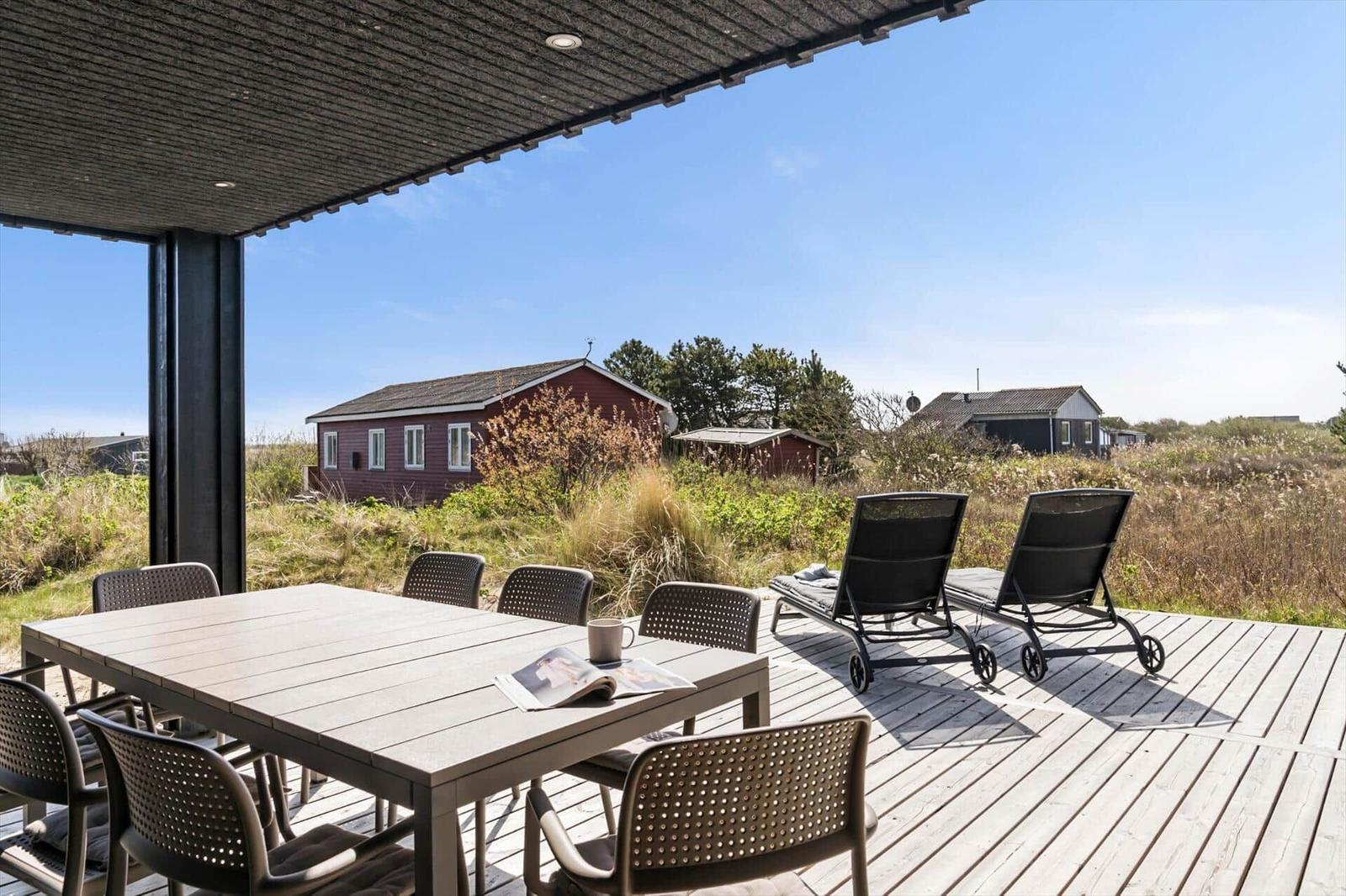 Terrasse mit Tisch, Stühlen und Liegen. Blick auf rote Häuser und Grasland.