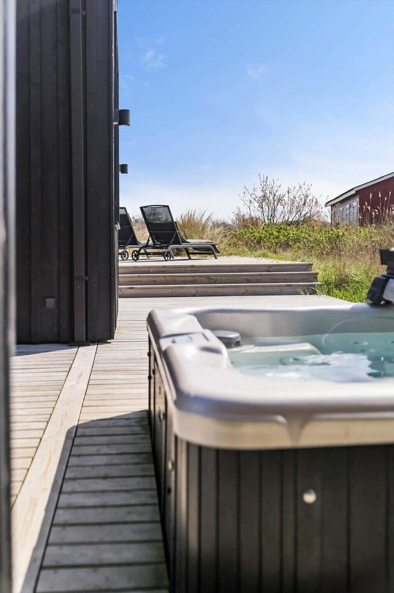 Hochwertiger Whirlpool auf Terrasse mit Liegestühlen und Blick auf Grünfläche.
