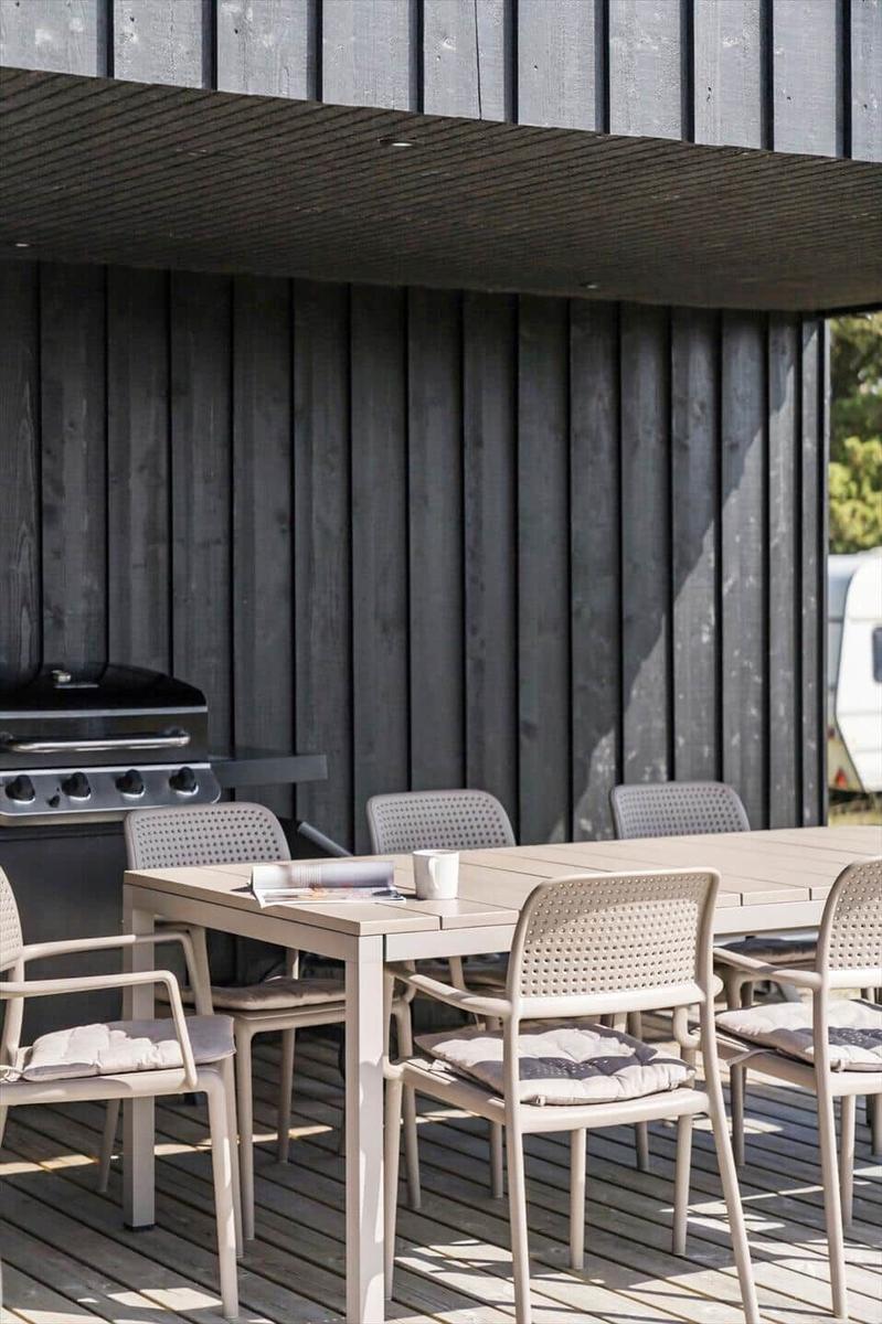 Terrasse mit Tisch, Stühlen und Grill an dunklem Holzhaus