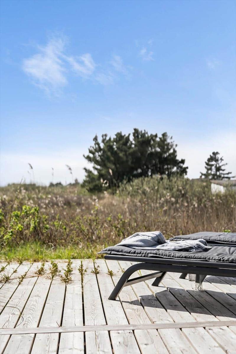 Liegemöbel auf Holzterrasse mit Blick auf Gras und Bäume unter blauem Himmel.
