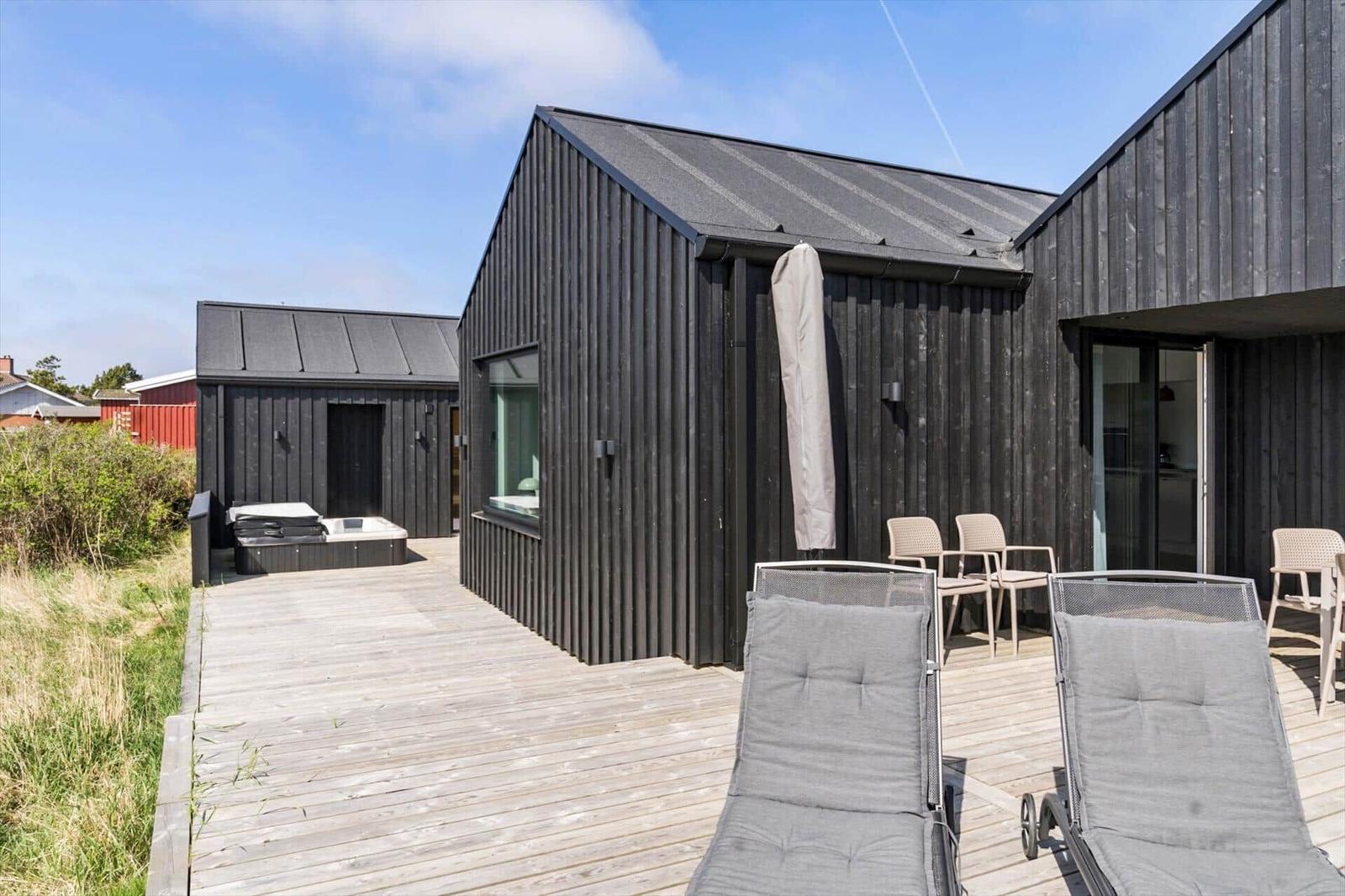 Modernes Holzhaus mit Terrasse, Liegestühlen und Whirlpool im Freien.