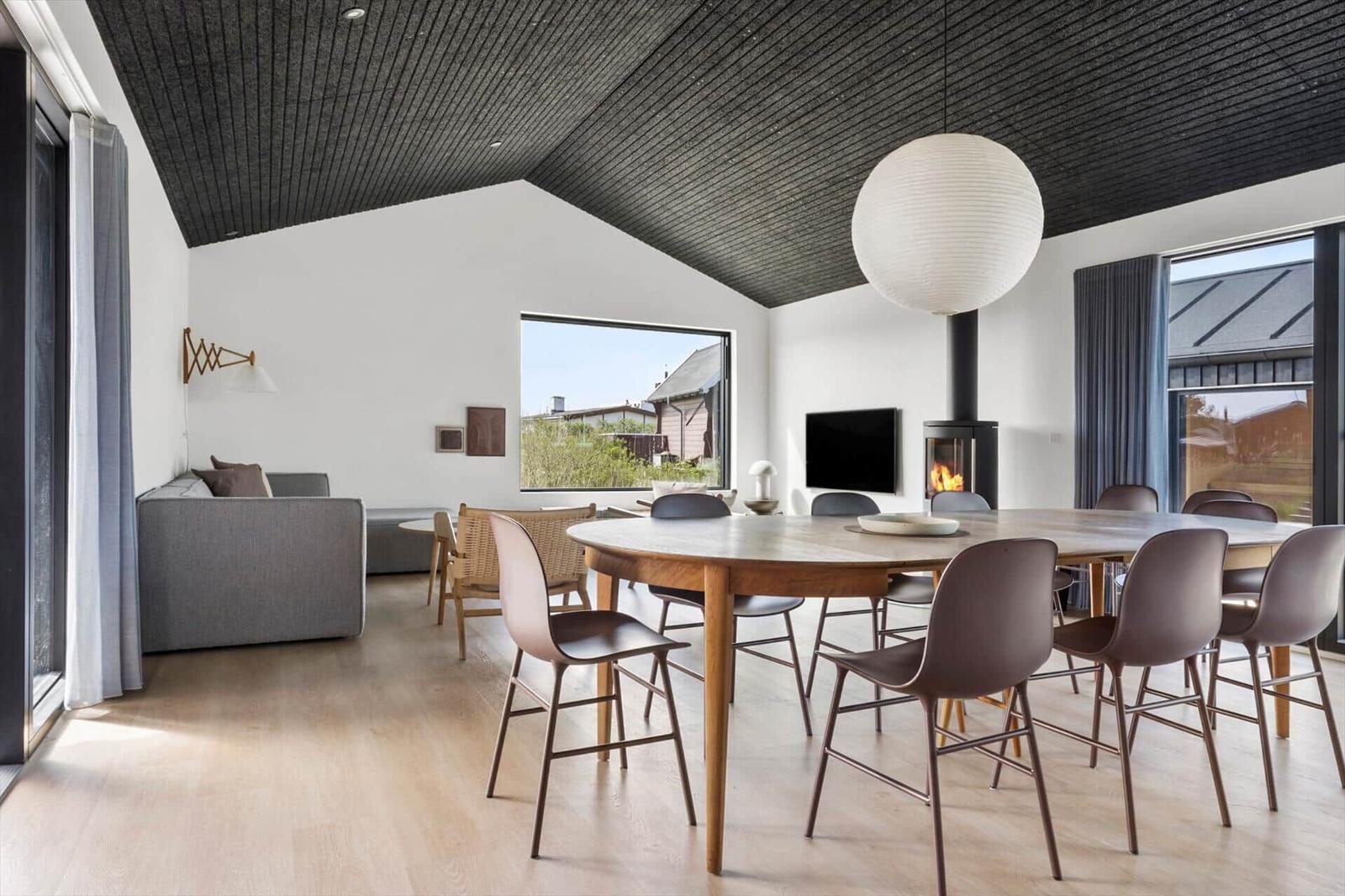 Ein Esszimmer mit runder Tisch und Stühlen. Hintergrund: Wohnbereich mit Sofa und Kamin.