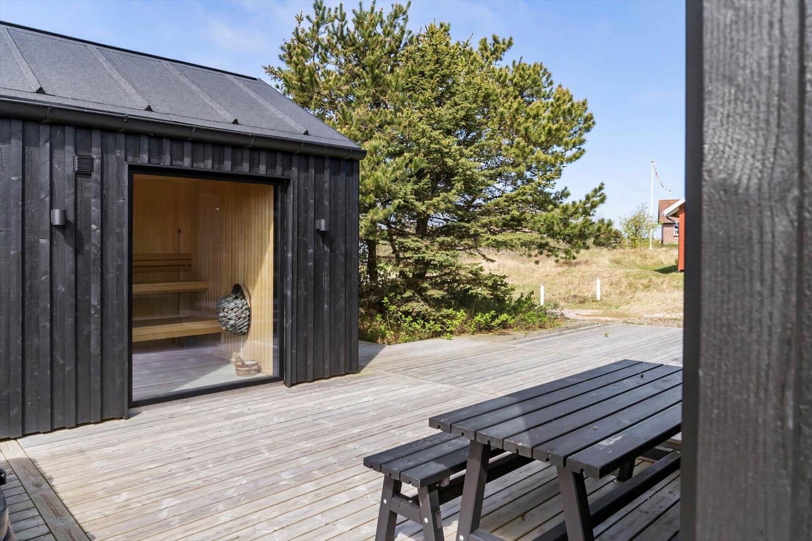 Außenbereich mit Sauna, Holzterrasse und Picknicktisch unter freiem Himmel.