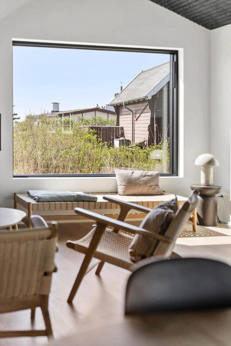 Großes Fenster mit Blick auf Garten und Nebengebäude. Holzstühle und Sitzbank mit Kissen.