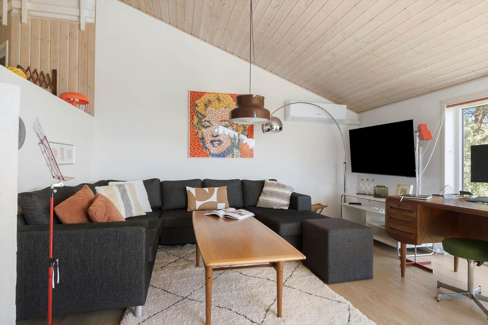 Wohnzimmer mit Sofa, Couchtisch und Wandbild. Holzdecke und Fenster mit Blick.