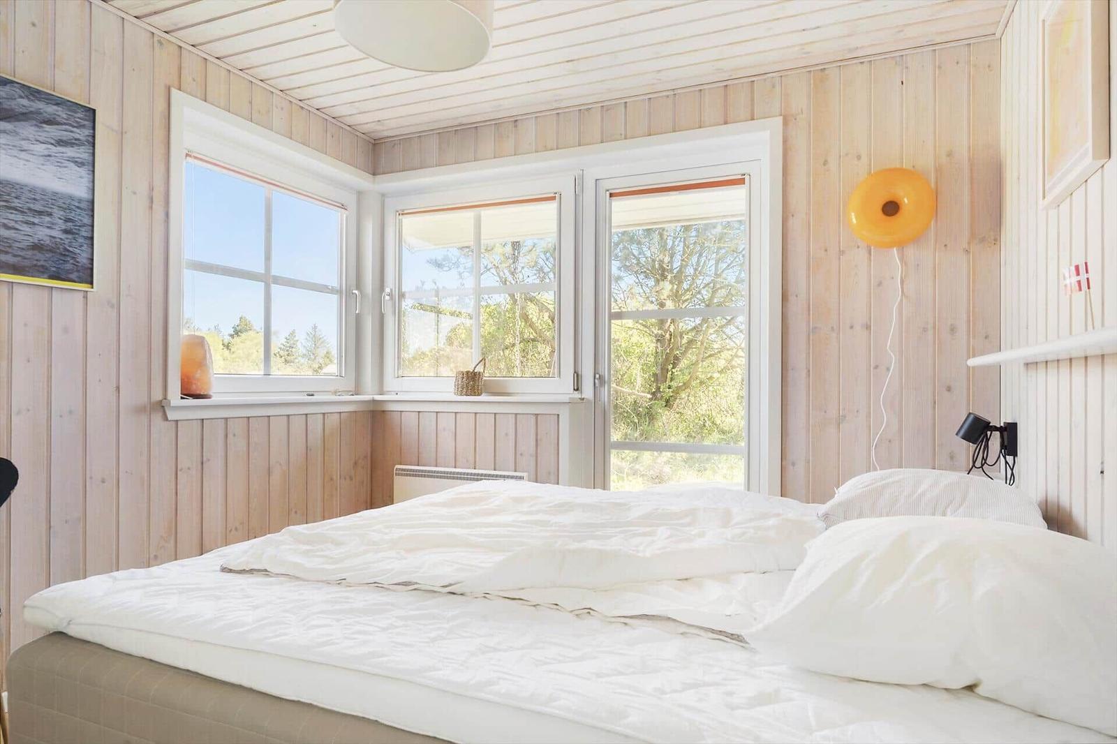 Schlafzimmer mit Holzwänden, Fenstern und Bett mit weißer Bettwäsche.