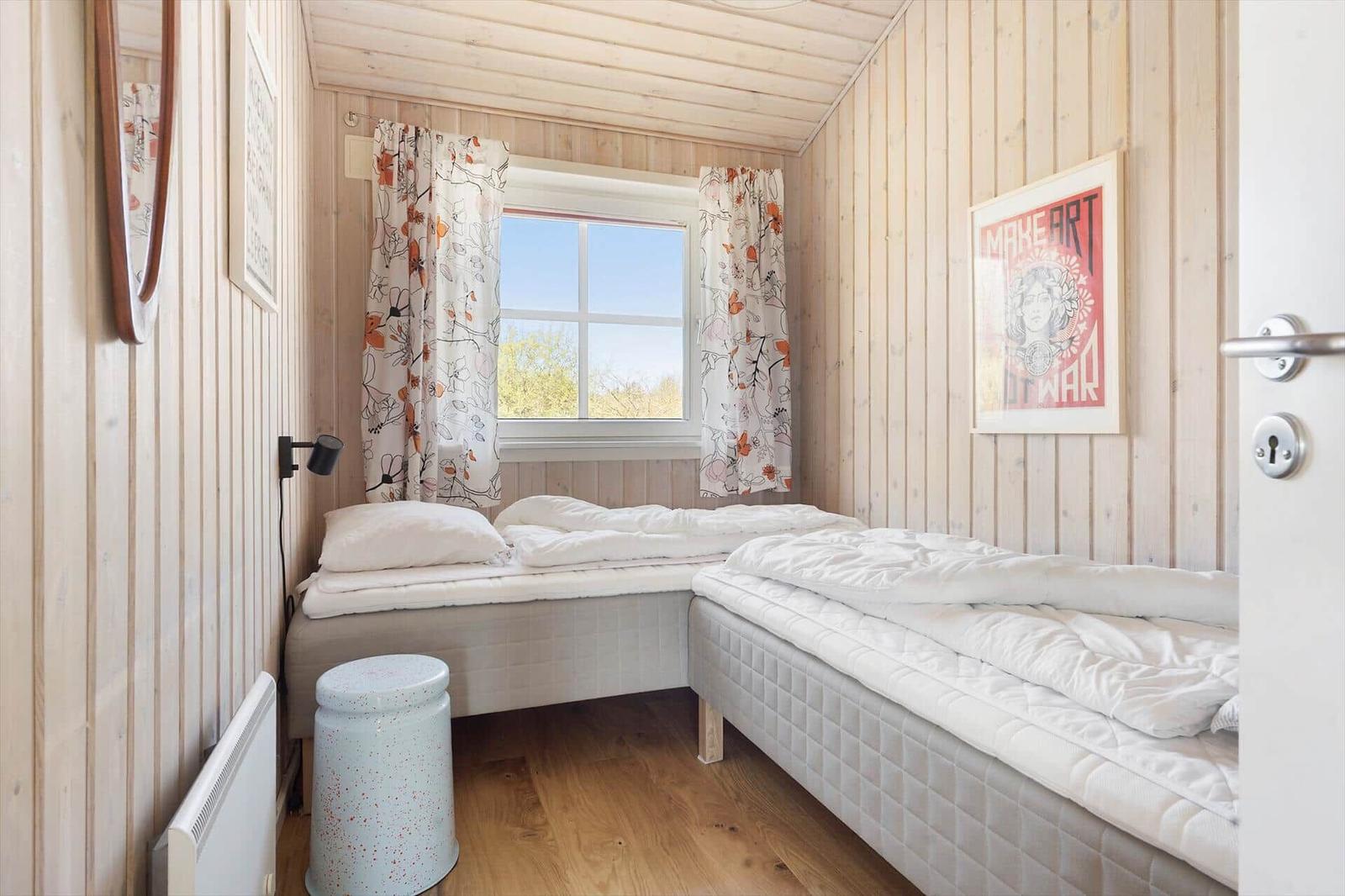 Zimmer mit zwei Betten, Holzwand und Fenster mit Vorhängen.