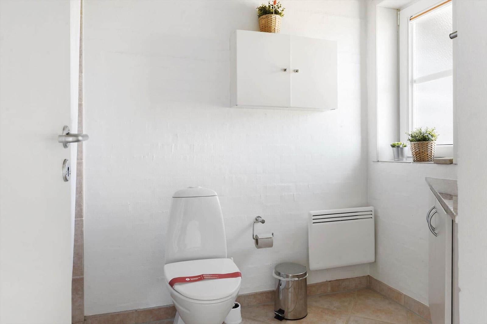 Badezimmer mit Toilette, Heizung und Fenster. Auf dem Fensterbrett stehen Pflanzen.