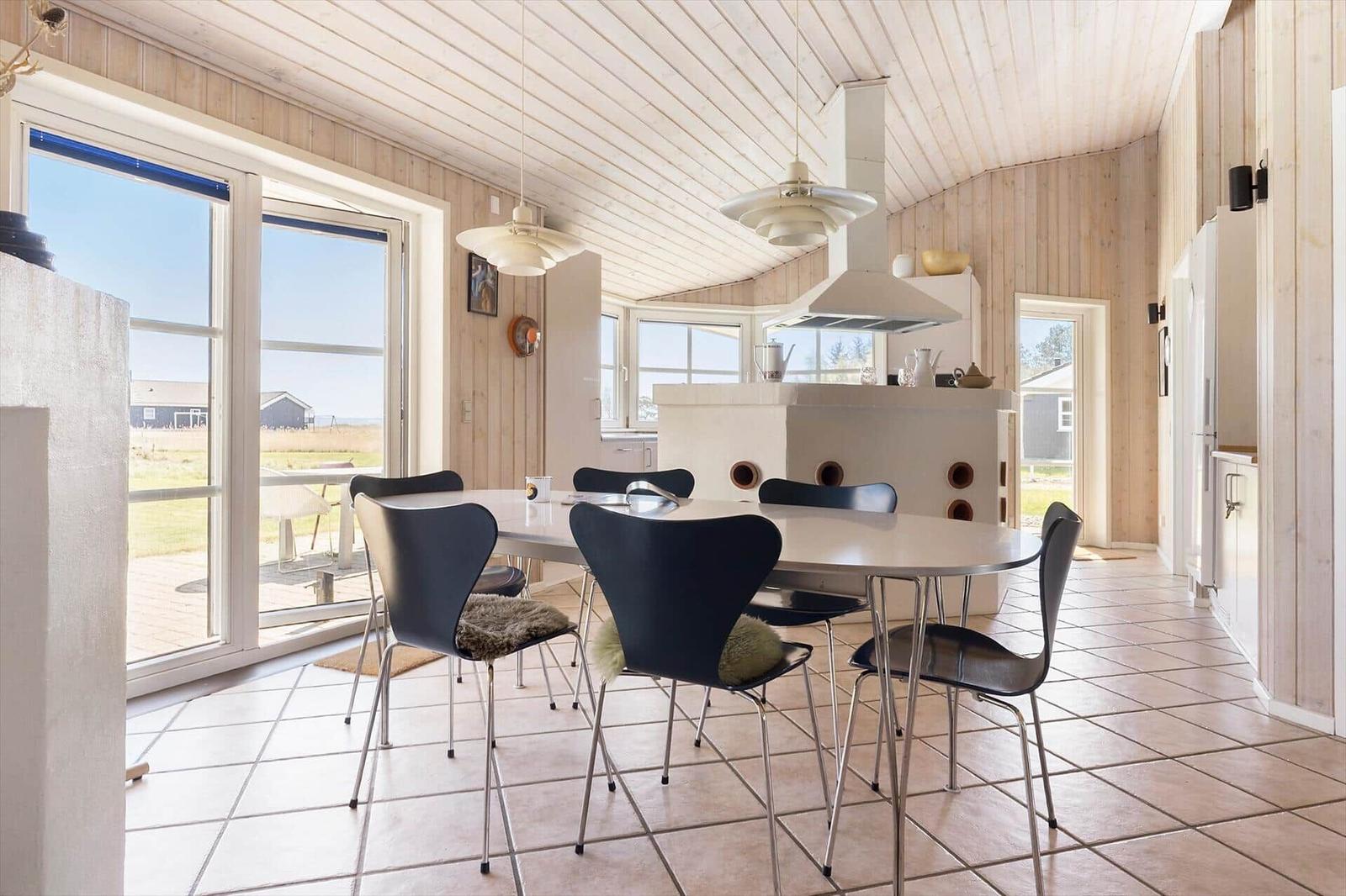 Essbereich mit runden Tisch und schwarzen Stühlen. Holzwände und große Fenster. Fliesenboden.