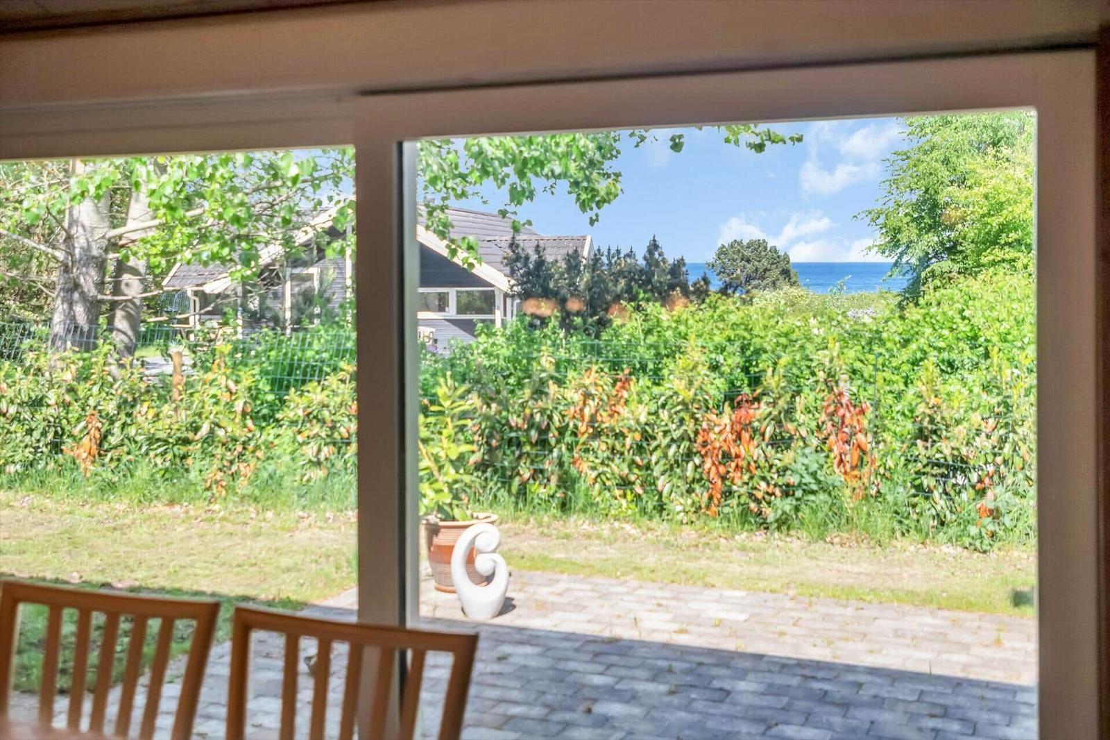 Durch die Glastür blickt man auf einen Garten mit Pflanzen und einen Blick auf das Meer.
