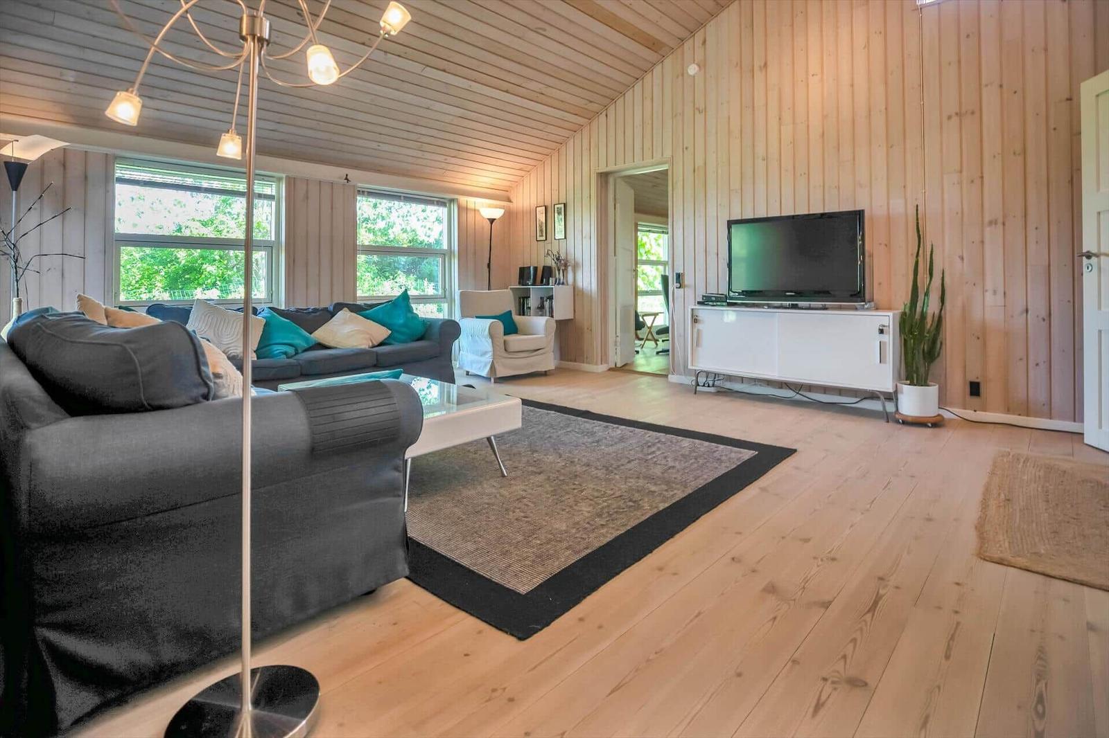 Wohnzimmer mit Holzwand, Sofa, Fernseher und großen Fenstern.