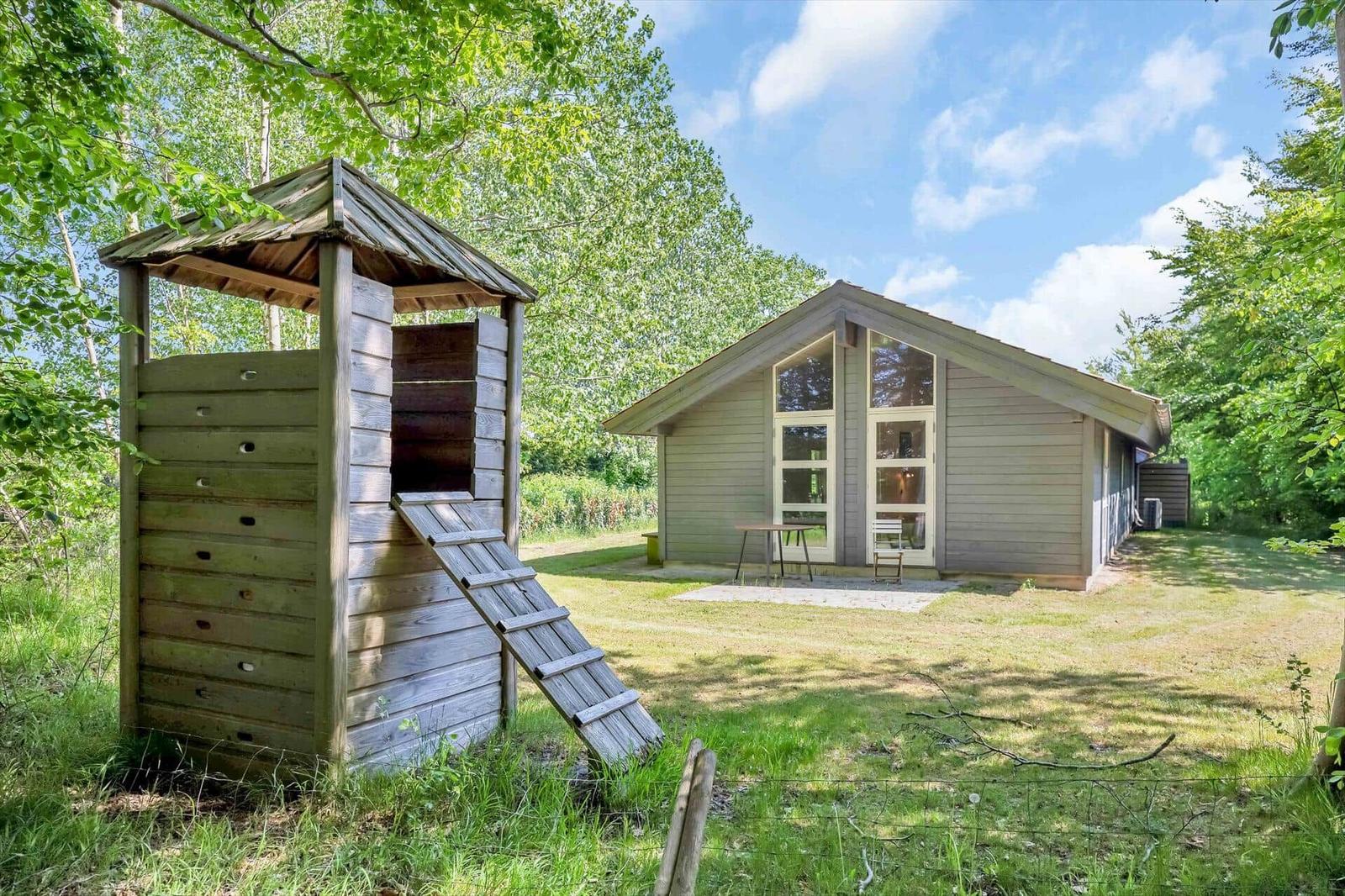 Haus mit Holzspielhaus und Garten unter Bäumen.